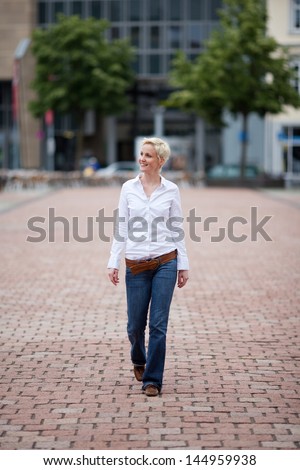Casual pretty young woman walking down an urban street with brick paving looking off to the left of the frame