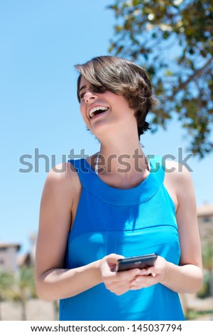Low angle view of a pretty vivacious woman laughing at the contents of an sms she has just received on her mobile phone