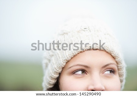 Daydreaming woman in a winter cap looking up to the top corner of the frame, cropped view of the eyes