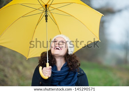 Happy Young Woman In Winter Clothes Holding Yellow Umbrella In Park