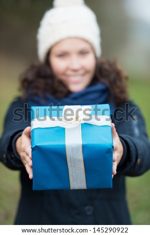 Young woman in winter clothes holding gift in park