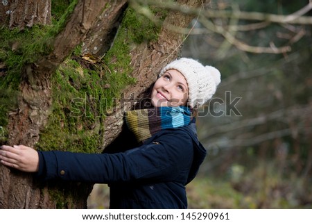 Young woman in winter clothes embracing tree in park
