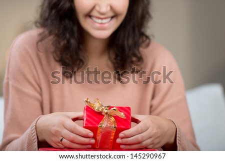 Excited woman with a small red gift box in her hands tied with a gold ribbon showing it to the camera
