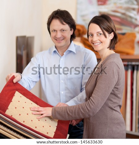 Woman searching for carpet samples standing looking at a sample book accompanied by a smiling young husband or salesman