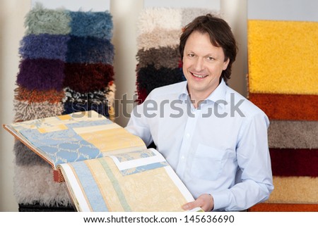 Friendly salesman with fabric and carpet samples in a book in his hands looking at the camera with a smile