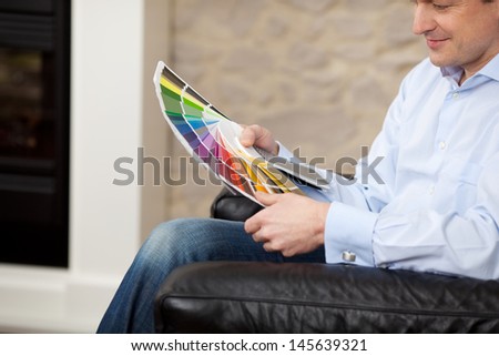 Man sitting in an armchair in his living room checking paint colors on a colorful set of color coded cards in his hands