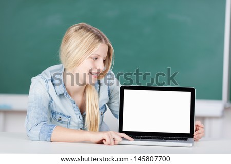 Young female student looking at blank laptop screen at desk in classroom