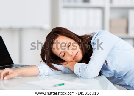 Tired businesswoman having a nap at her desk with her head lying on her arm facing the camera