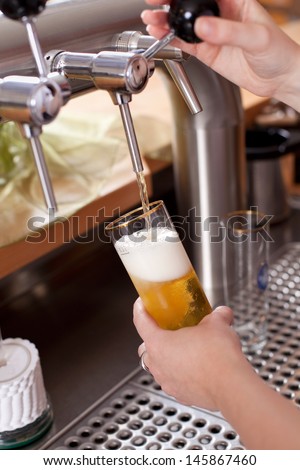 Waitress dispensing draft beer into a pint glass from the metal spigot on a keg in the bar