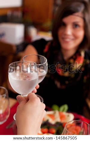 Two women toasting in a restaurant with wineglasses filled with chilled mineral water, focus to the glasses