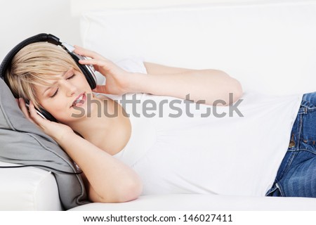 Woman wearing headphones listening to music lying on her back on a sofa with her eyes closed in enjoyment and appreciation