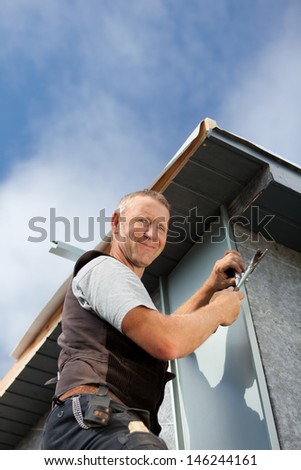 Smiling roofer assembles a metal piece on a dormer wall