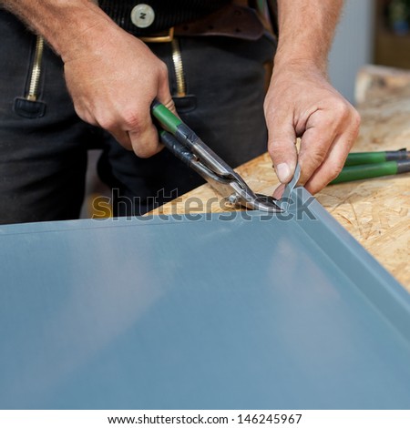 Close-up of a roofer making cuts on a metal sheet using cutting pliers and removing the excess material