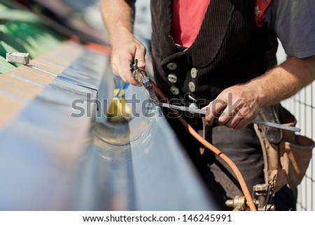 Close-up of a roofer applying weld into the gutter parts to assemble it