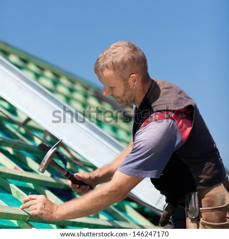 Roofer hammering nails into roof beams for the construction of the roof