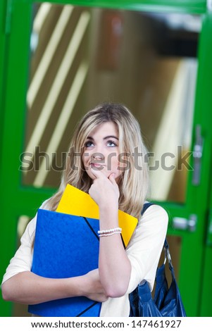 Confused female student holding files while standing against door in school