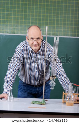 Portrait of confident male professor leaning on desk in science class