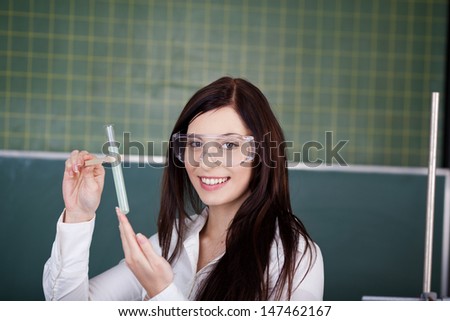 Portrait of happy young female student holding test tube with clamp against chalkboard in classroom