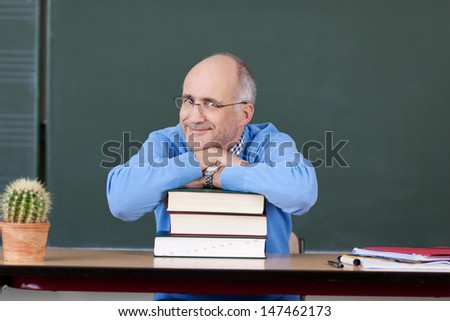 Portrait of male professor relaxing on stacked books at desk in classroom