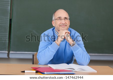 Thoughtful male professor with hands on chin looking up at desk in classroom