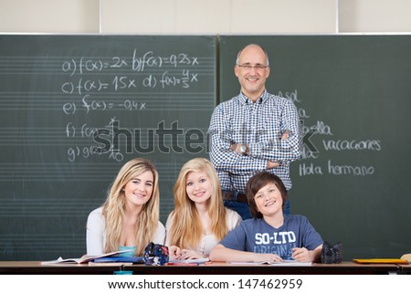 Portrait of confident professor and students smiling together against chalkboard in classroom