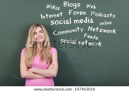 Happy teenage girl looking at collection of social media and networking related words on blackboard