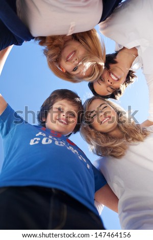 Low angle portrait of children and teacher forming huddle against clear blue sky