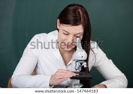Young female student using a monocular microscope looking at test slides under the objective