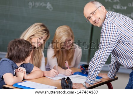 Friendly male teacher in the classroom looking back over his shoulder at the camera with a smile while teaching three young students