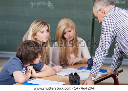 Male teacher giving a lesson to two young girls and a boy seated at a desk