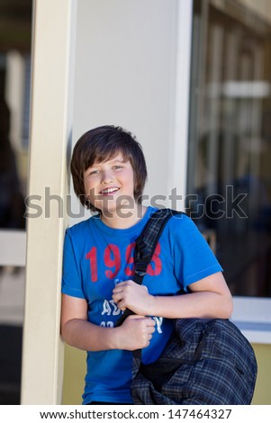 Happy young boy going to school with a large bag of books slung over his shoulder grinning at the camera