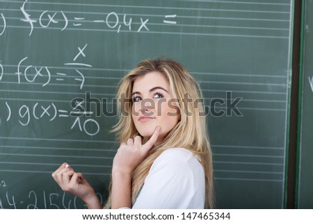 Thoughtful young girl trying to find a solution to a maths problem in the classroom standing in front of the equation on the chalkboard