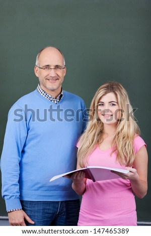 Portrait of a mature male teacher and attractive teenage female student standing together in front of the blackboard in the classroom
