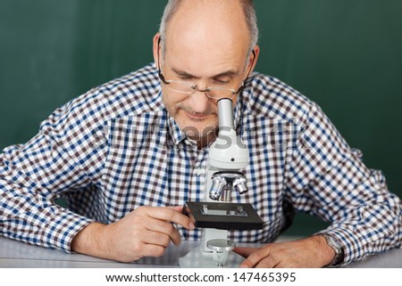 Middle-aged balding man wearing glasses looking down a microscope at a glass slide with a specimen