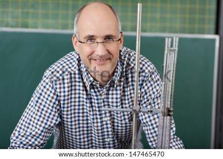 Close up portrait of a middle-aged male teacher in glasses giving physics lessons standing in front of a metal retort stand used in an experiment