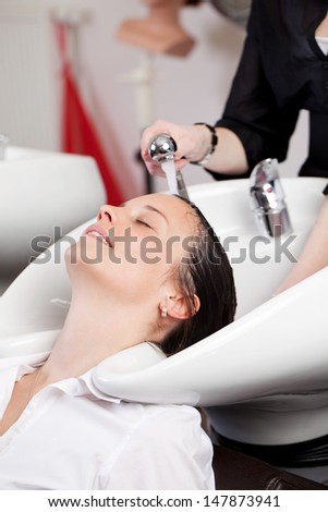 Hairstylist giving a hair shampoo at a hand basin in the hair salon to a relaxed woman customer