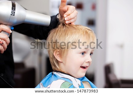 Little child with a look of comical amazement getting a blow dry at the hairdresser from a professional stylist