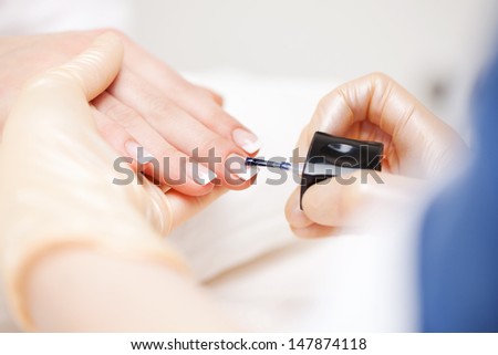 Manicure in a beauty salon with a beautician applying clear nail varnish to the elegant finger nails of her client