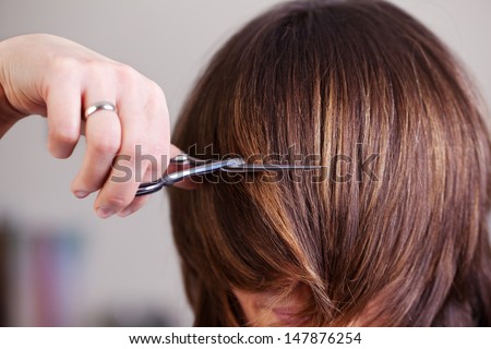 Woman with mid length brunette hair having her hair cut short at a hair salon by a stylist using scissors
