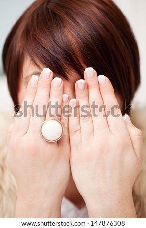 Woman with manicured French nails holding up her hands on display in front of her face and wearing a ring with a large circular white gemstone of generic design