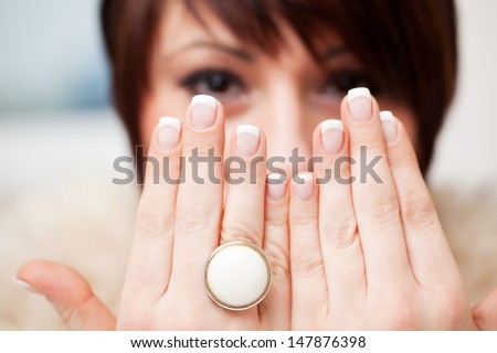 Woman displaying her manicured nails holding up her hands in front of her face and wearing a ring with a large circular white gemstone of generic design