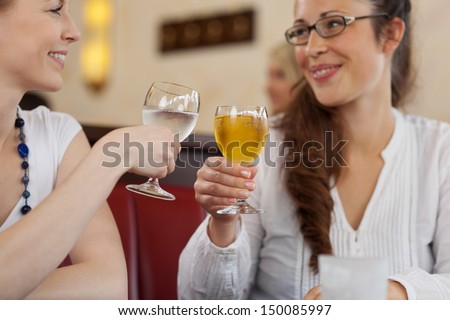Two female friends toasting each other with chilled drinks in a restaurant smiling as they celebrate together