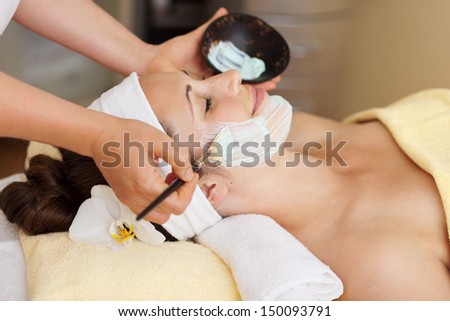 Therapist applying a face mask to a beautiful young woman in a spa using a cosmetics brush