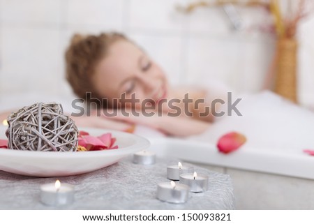 Beautiful woman soaking in a bubble bath with her eyes closed in bliss with focus to the candles in the foreground