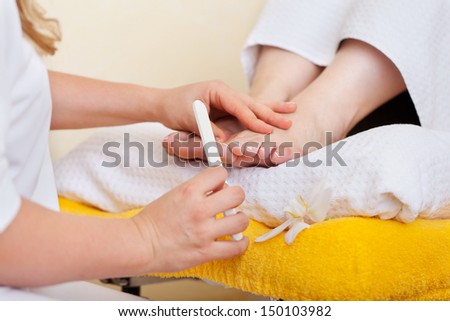Pedicurist performing a pedicure in a salon carefully filing a womans toenails with a nail file, close up view