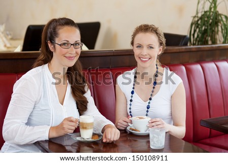 Two beautiful women in a cafe sitting at a table together drinking cappuccino coffee and macchiato