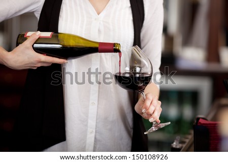 Close up of the hands of a young woman pouring red wine into a glass from a bottle