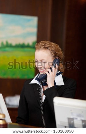 Young female receptionist smiling while answering the telephone at the reception desk of a hotel