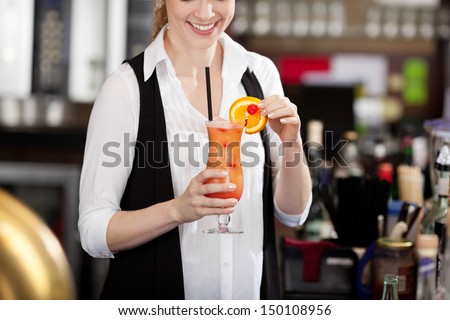 Female bartender making a tropical fruit cocktail holding an elegant long glass of beverage in her hand as she adds the sliced orange garnish to the rim