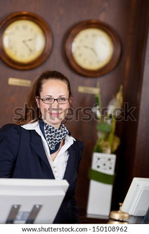 Stylish female receptionist standing behind a reception desk in an international venue ready to serve you on her computers